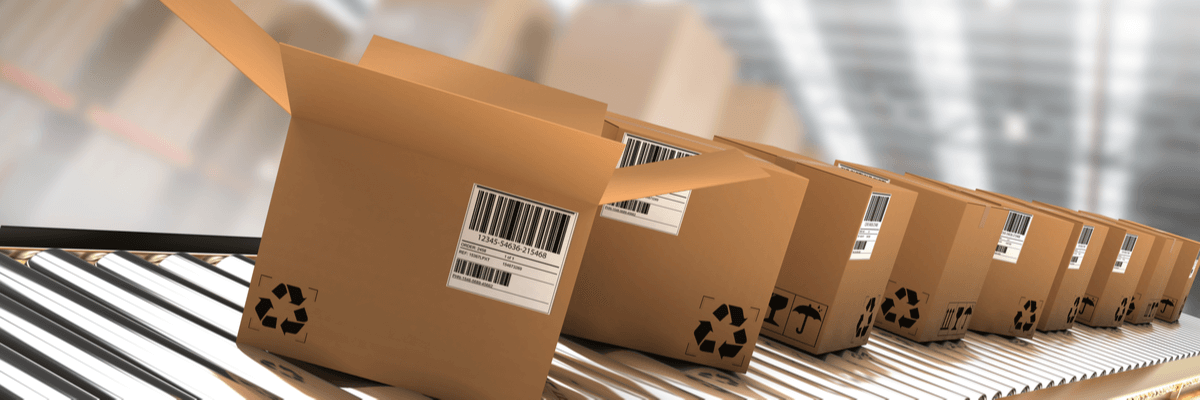 Row of brown boxes with labels on conveyor belt against boxes in illuminated warehouse, manufacturing industry concept or warehouse