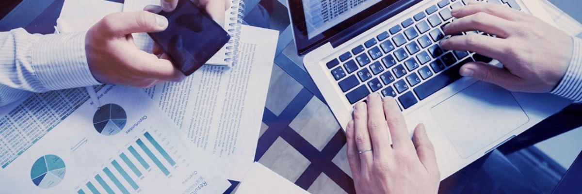 Close up of hands on a laptop, paperwork or files on the desk, another business man with a cell or mobile phone in hand