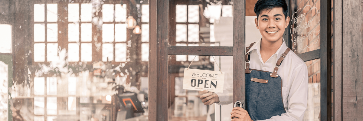 Store owner turning open sign broad through the glass door, ready to service.